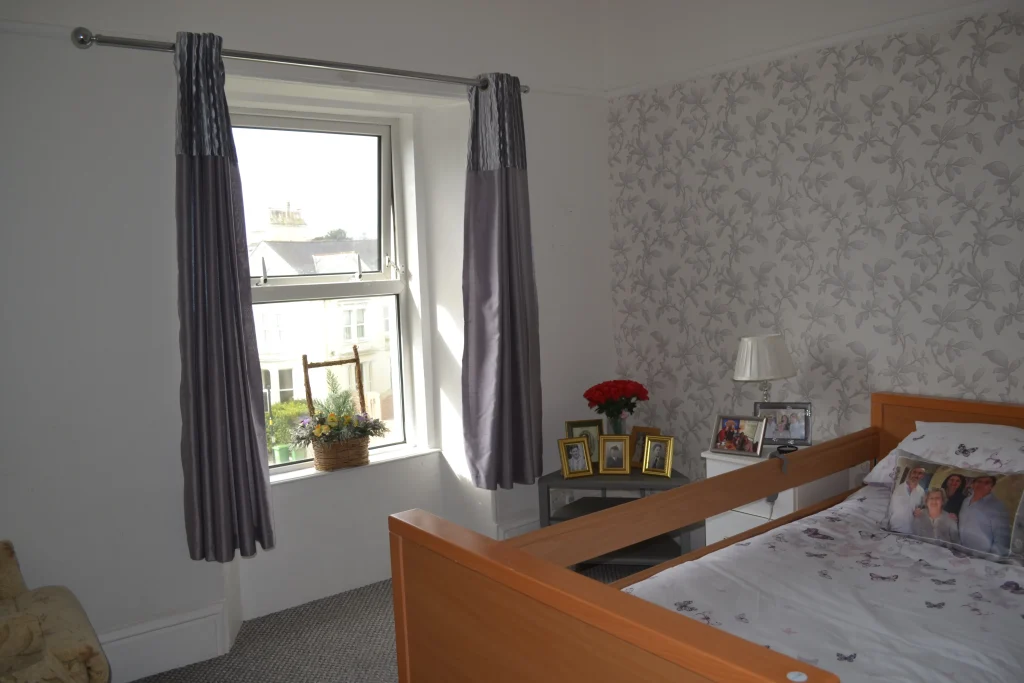 A bedroom at Chatsworth with grey curtains, family photographs on the bedside table and a profiling bed