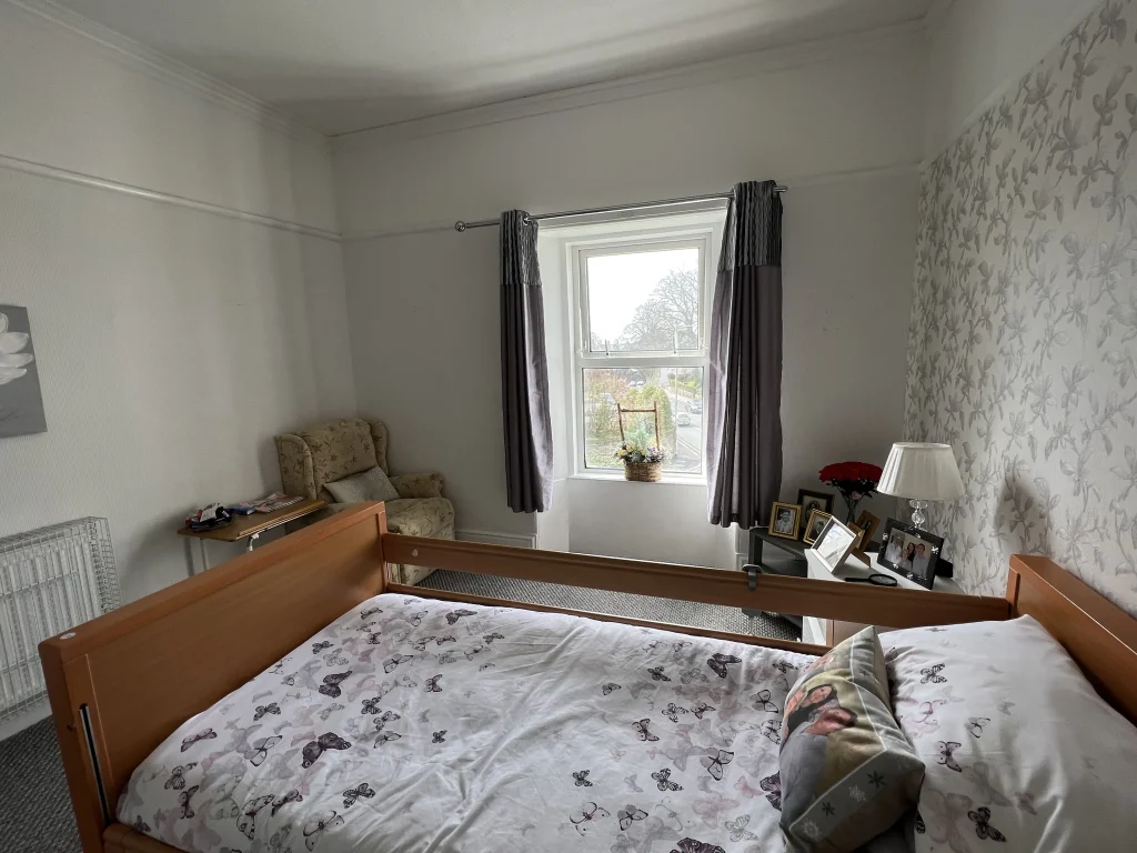 A bedroom at Chatsworth with a profiling bed, patterned wallpaper and a window looking over the road